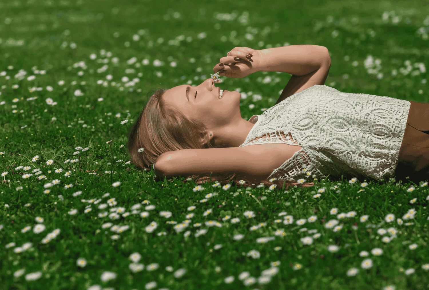confidence-happy-exercise woman lying in grass smelling a daisy to demonstrate the joy of building confidence during the summer