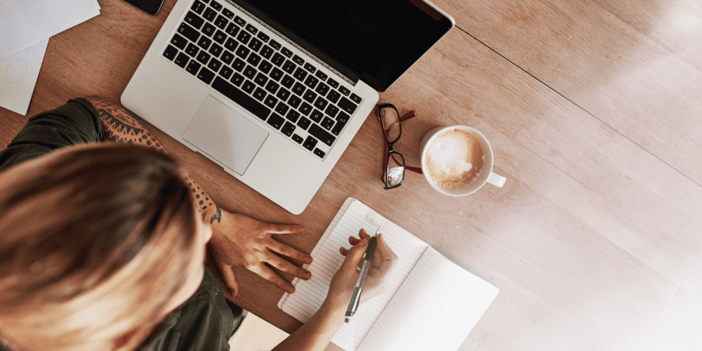 how-to-achieve-goals Woman writing in a notebook to demonstrate writing down your Magic 20 list to achieve your goal