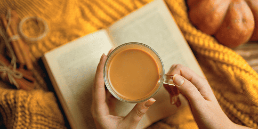Hands holding a cup of coffee and a book to demonstrate the importance of reading books that inspire you to stay motivated
